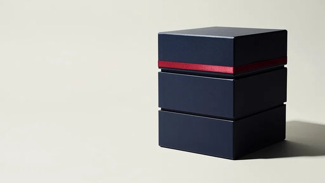 A stack of three matte navy archive boxes on a pale grey studio background, sealed with a single thin red band.