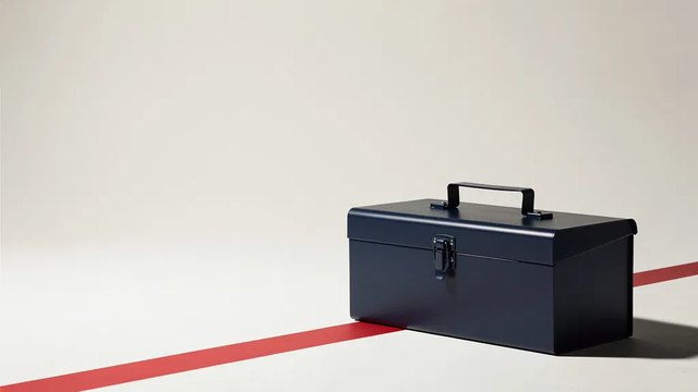 A closed navy metal toolbox on a pale studio floor with a red stripe running diagonally behind it.